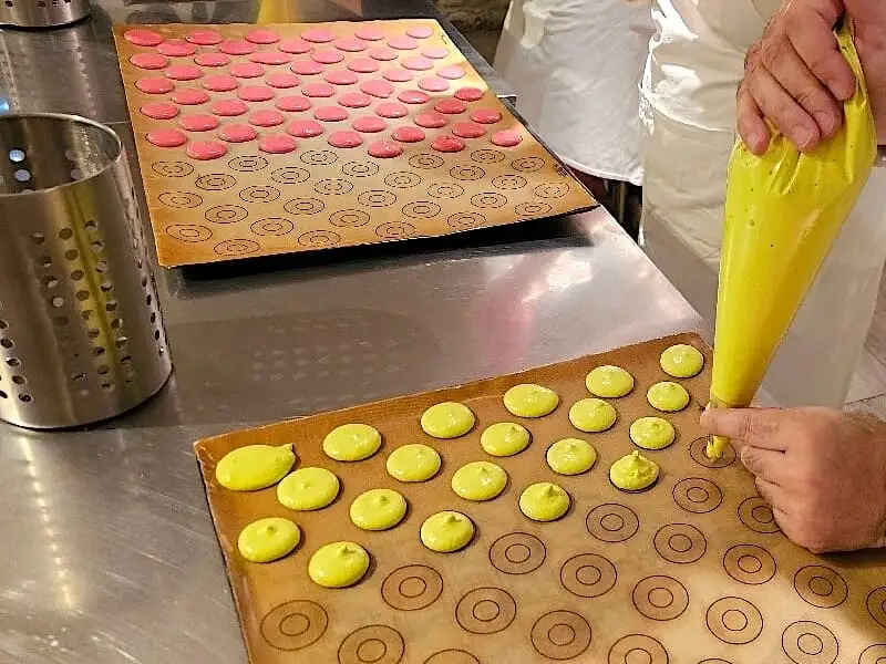 Superficie de trabajo con pequeños macarons y una manga pastelera